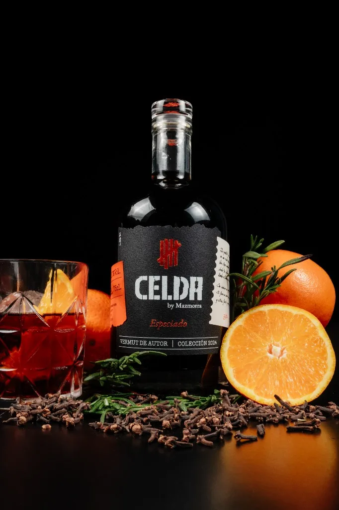 Botella de Vermut Celda Especiado con tapón de cristal, rodeada de clavo, romero y naranja, y vaso servido con hielo