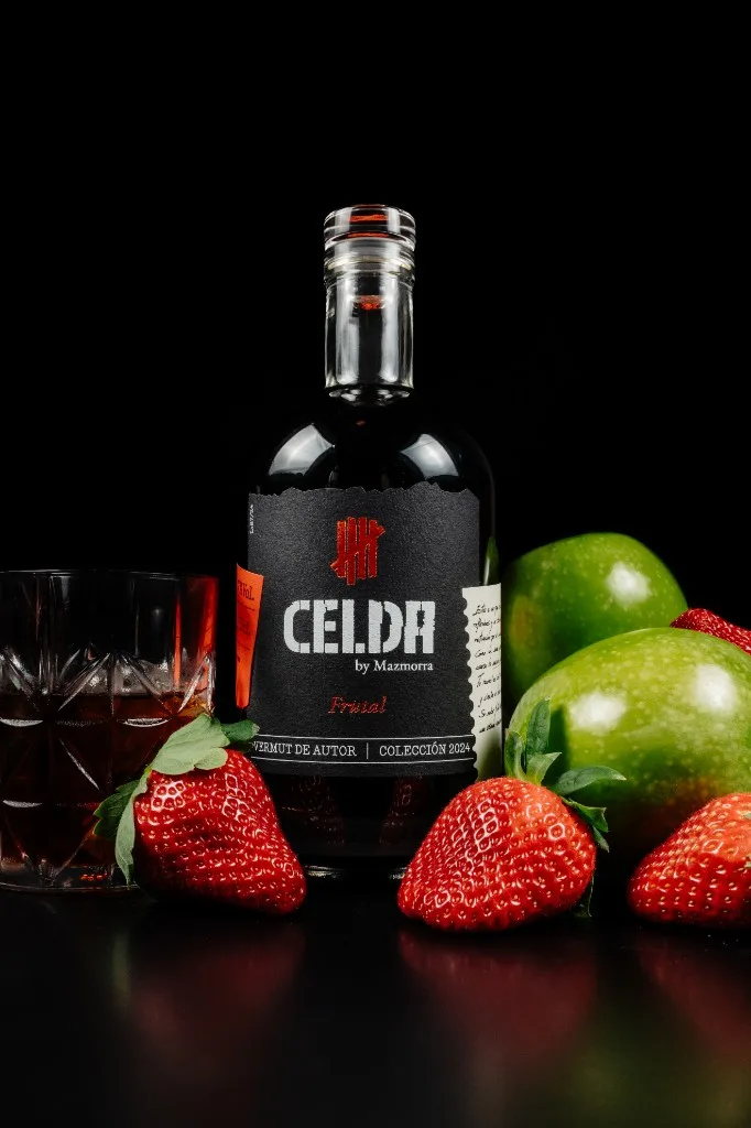 Botella de Vermut Celda Frutal con tapón de cristal, rodeada de fresas y manzanas verdes Granny Smith, y vaso servido