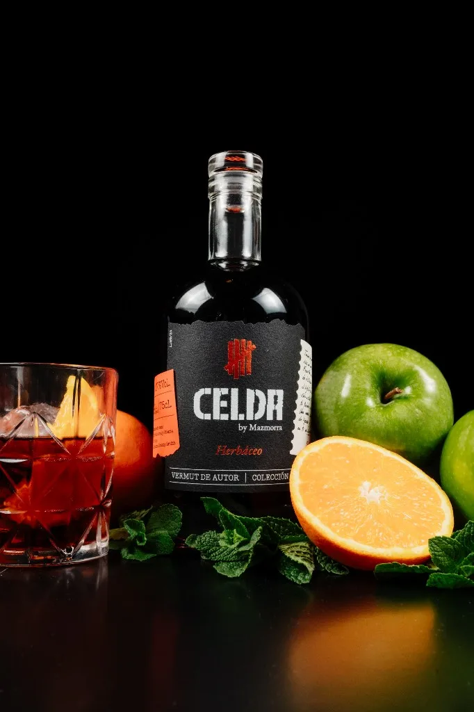 Botella de Vermut Celda Herbáceo con tapón de cristal, rodeada de hierbabuena, menta, naranja y manzana verde, y vaso servido